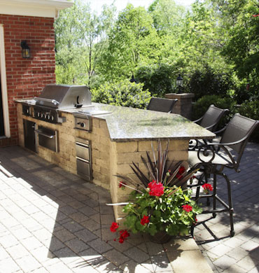 An outdoor residential entertainment space featuring an exterior kitchen for preparing food and highchairs for seating