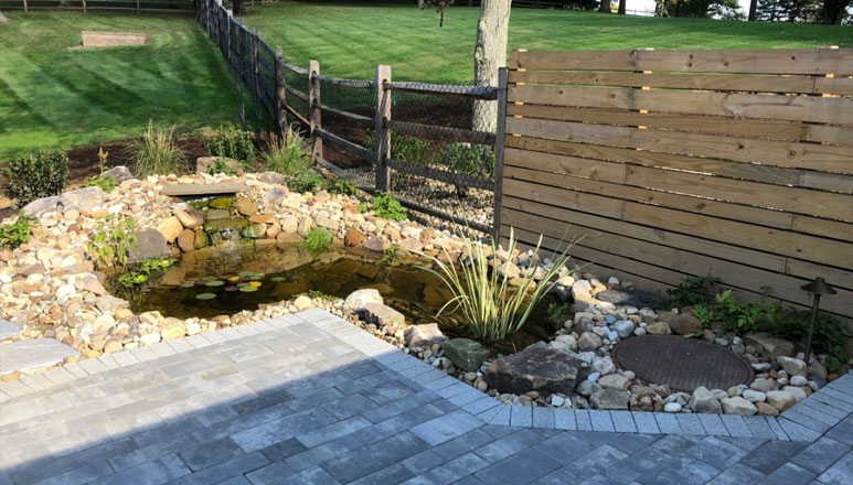 A backyard stone masonry patio showcasing a lily pond and decorative fencing