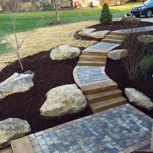 A residential masonry walkway accented with boulders and fresh mulch