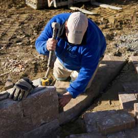 A blue fox landscape design laborer installing a masonry retaining wall
